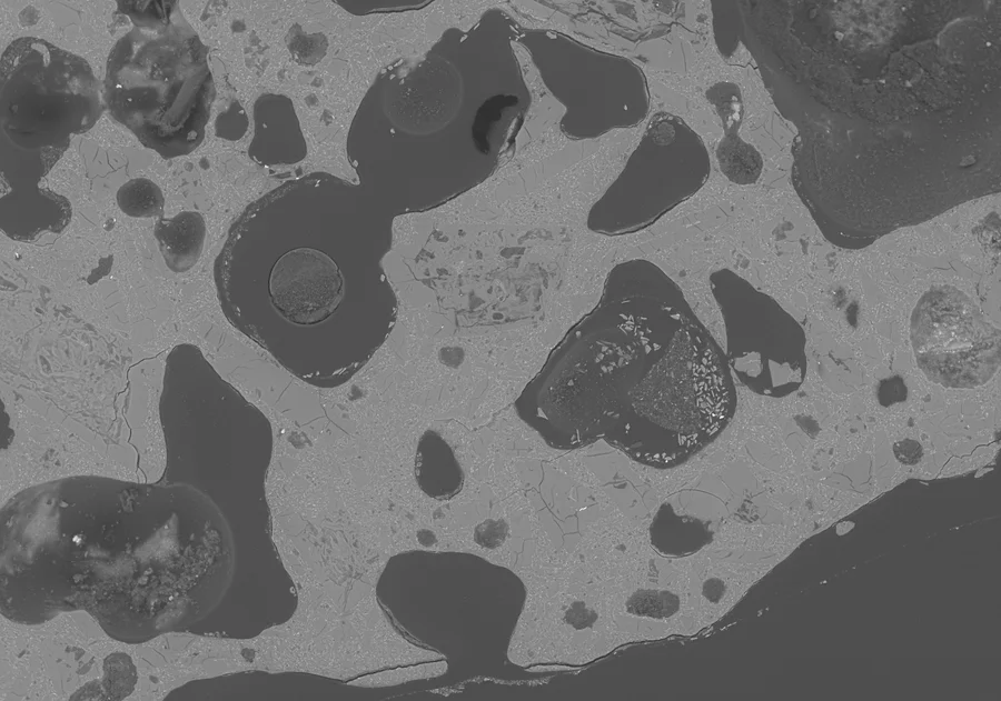Grayscale scanning electron microscope image showing vesicles and solid material in a pyroclast sample.